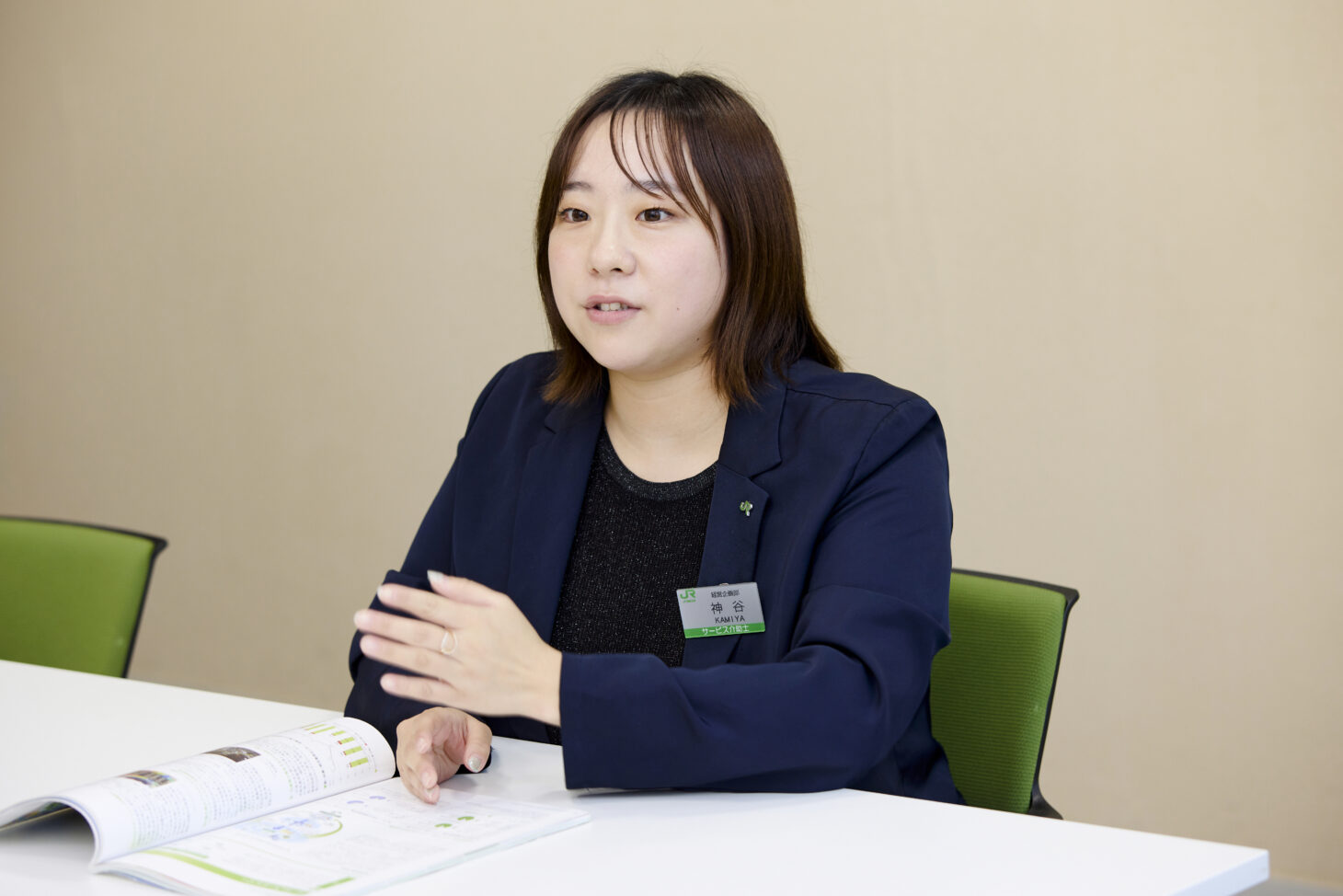 開いた資料が置かれた白い机の前で取材に応じている神谷葵さん